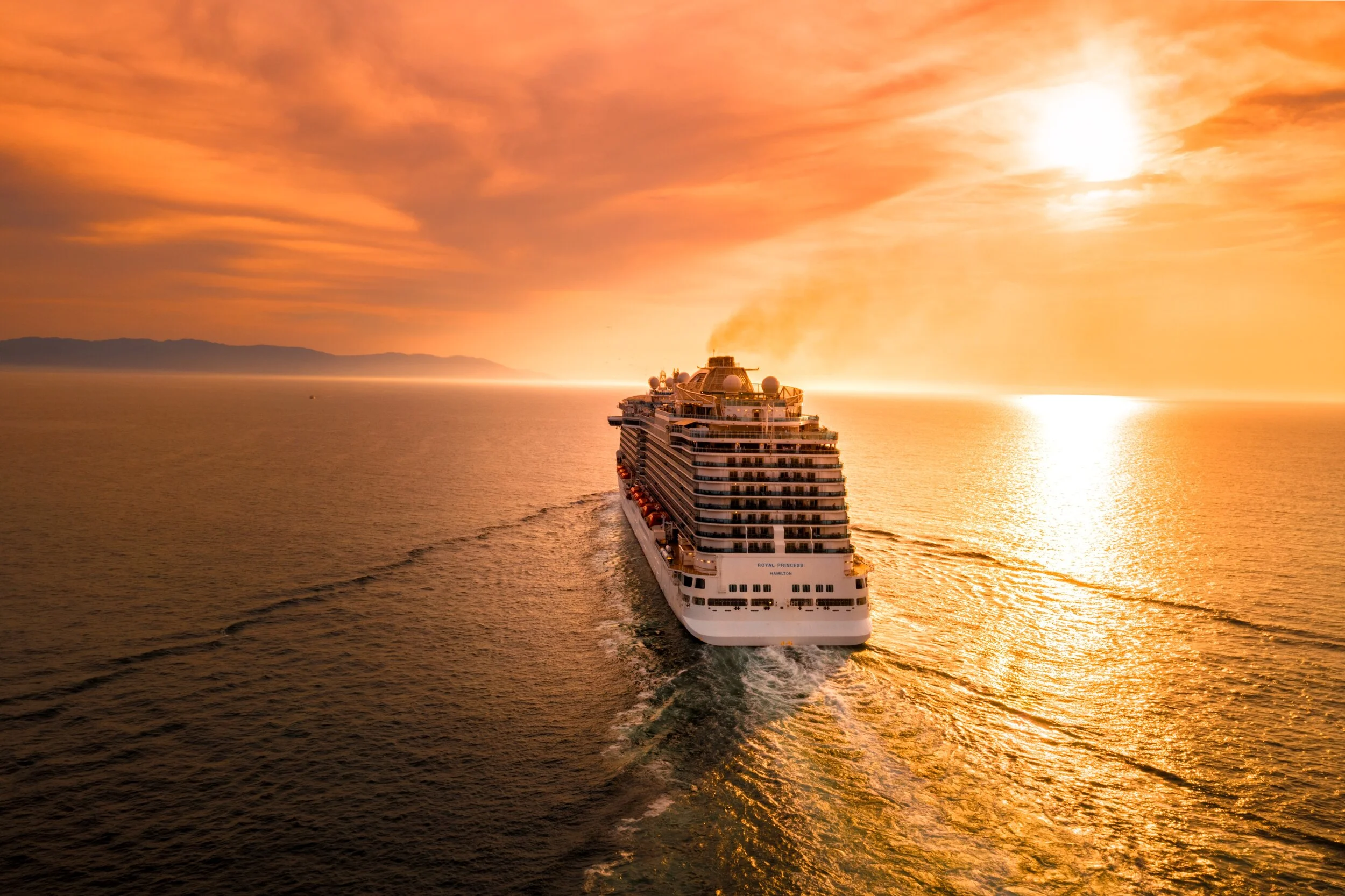 Cruise ship sailing towards horizon at sunset