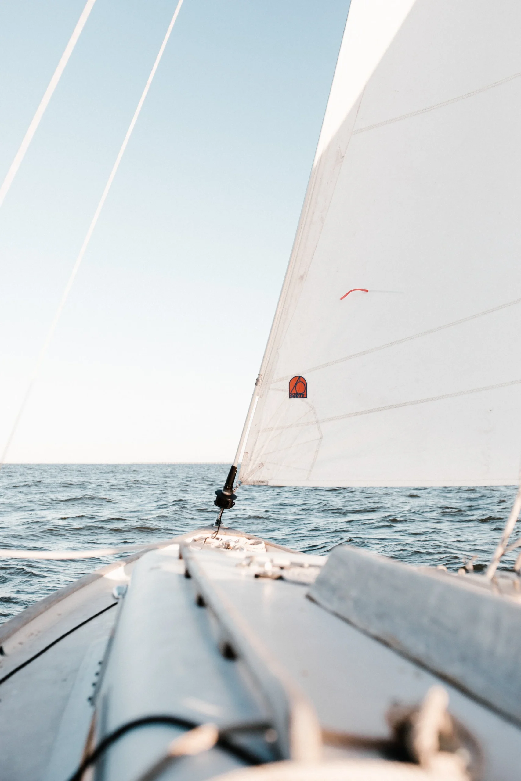 View from a sailboat with an ocean horizon and clear sky.
