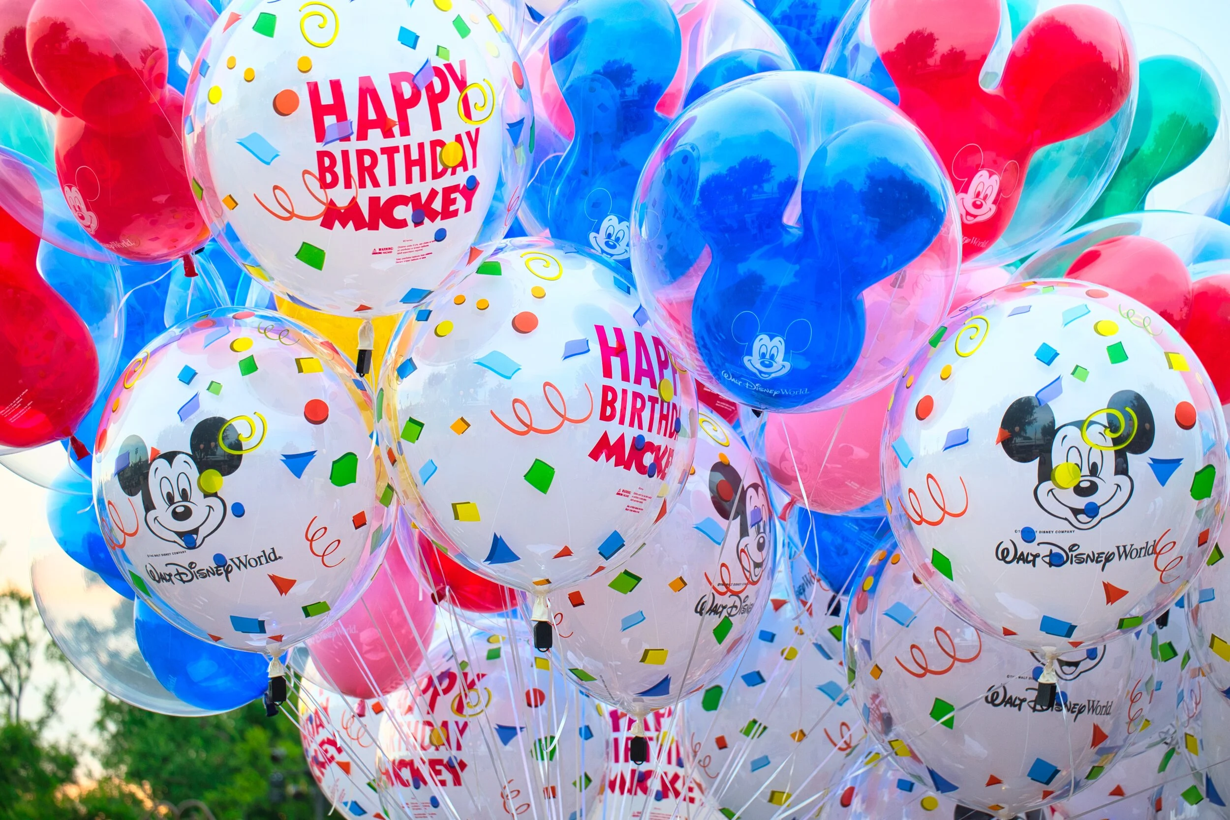 Cluster of colorful Mickey-themed balloons, including transparent and foil designs, celebrating "Happy Birthday Mickey," with Disney branding.