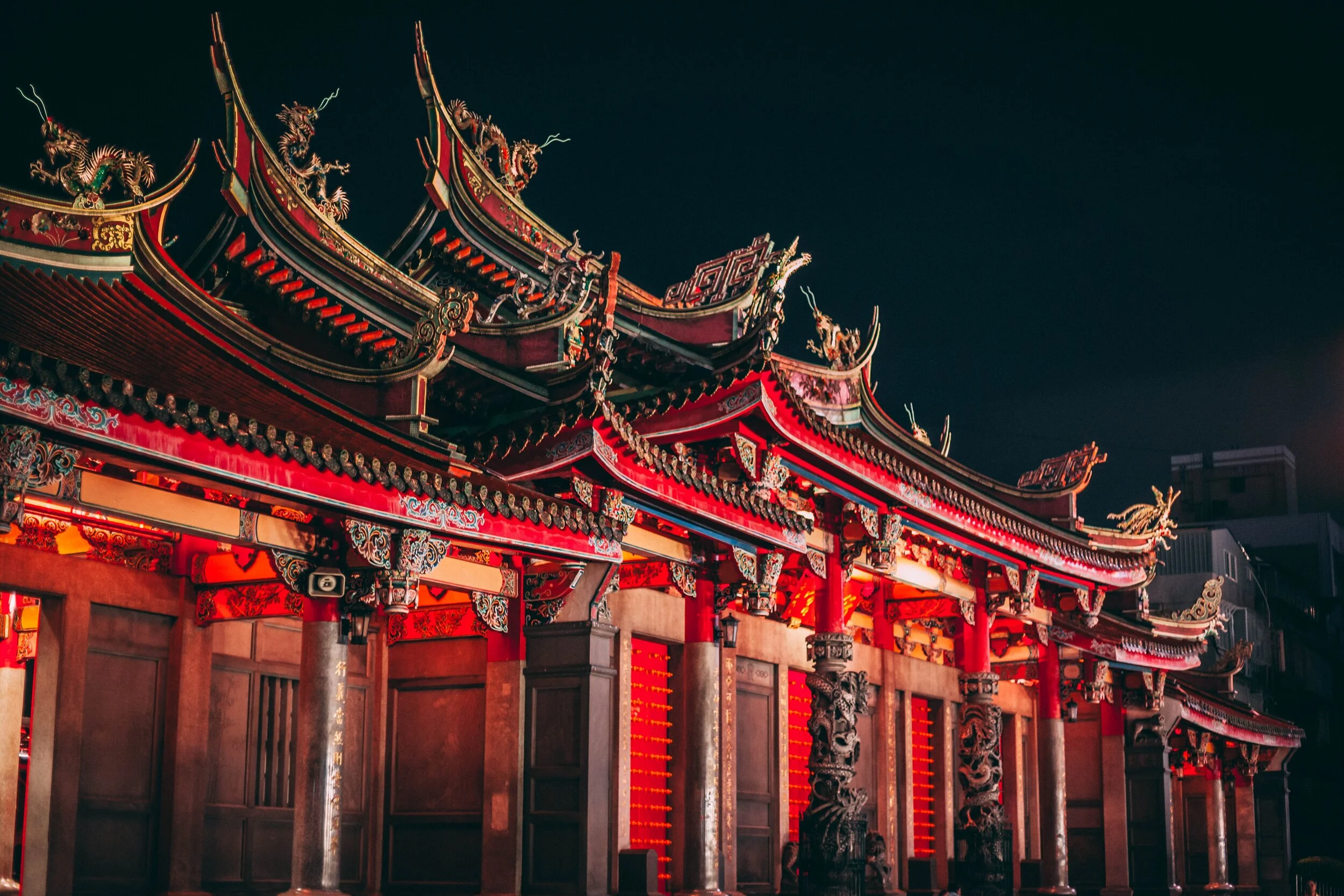 Traditional Chinese temple with intricate red and gold architectural details and dragon sculptures, illuminated at night.