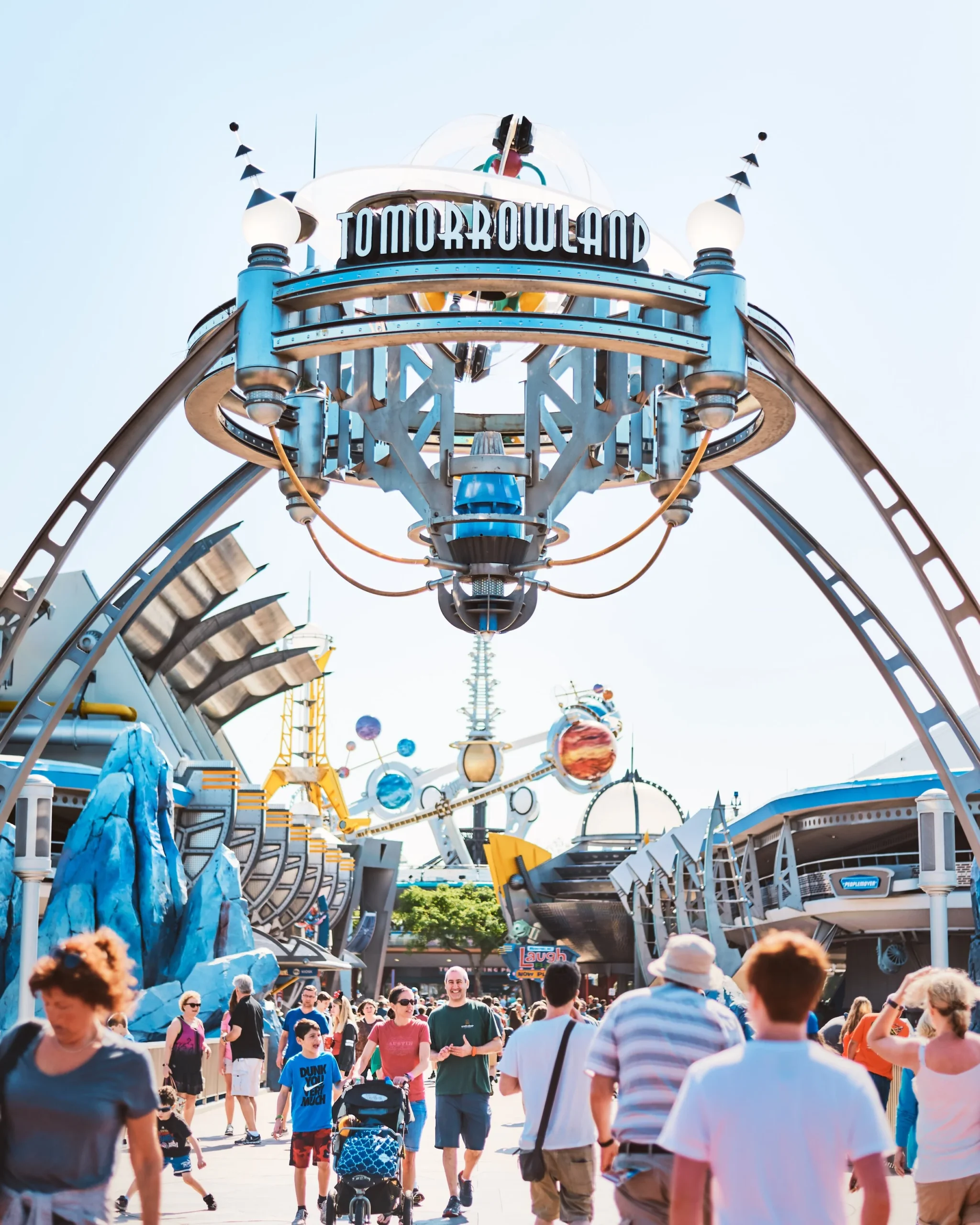 Entrance to Tomorrowland at a theme park with futuristic architecture and people walking underneath.