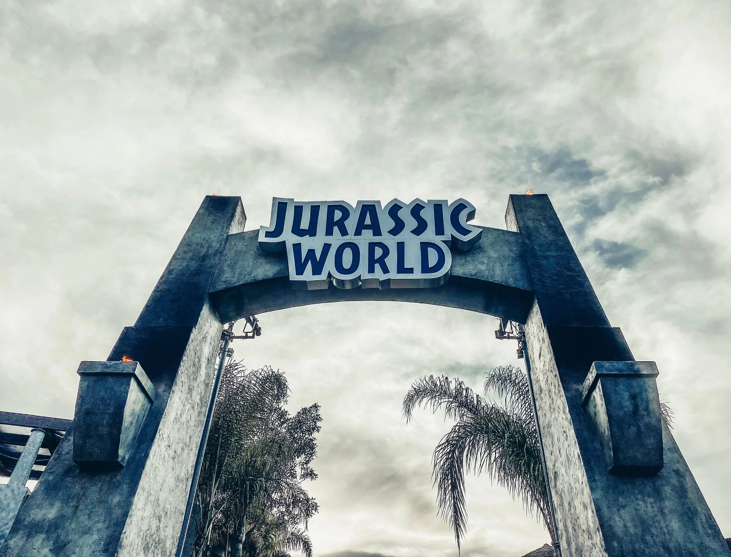 Entrance archway with 'Jurassic World' sign against a cloudy sky.