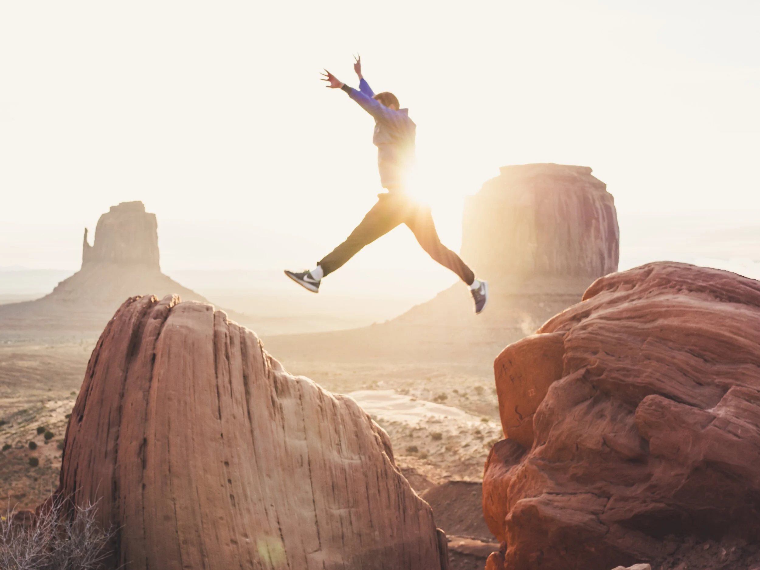 Person jumping between red rock formations in a desert landscape at sunrise or sunset.