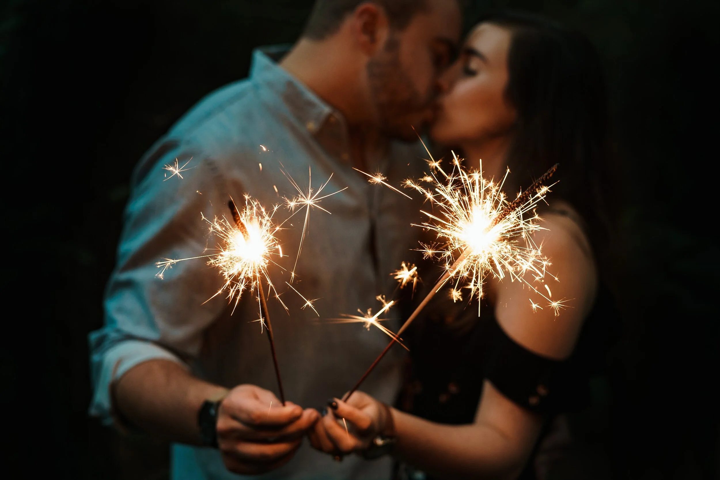 Couple kissing while holding lit sparklers.