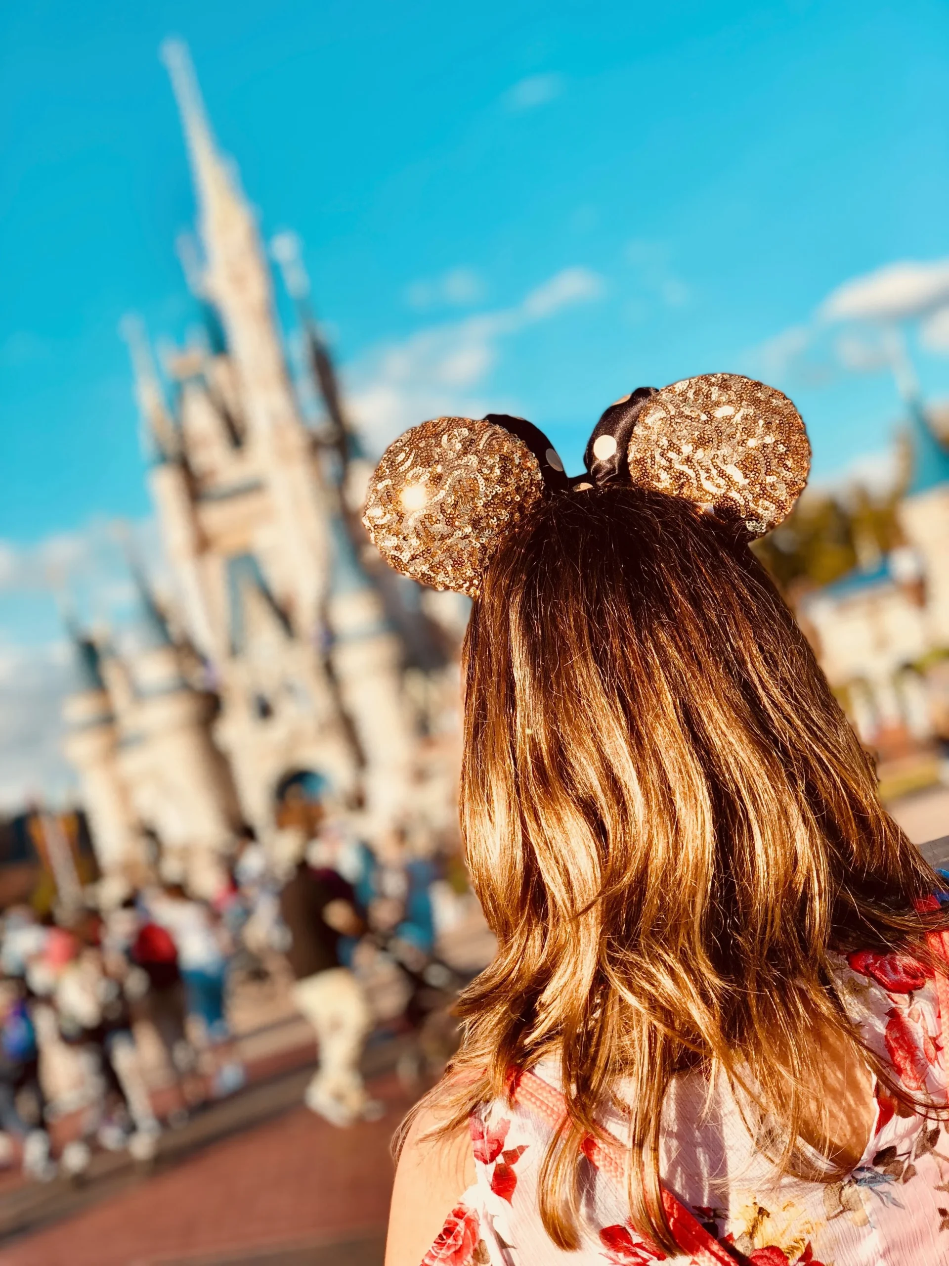 Person wearing sequin Mickey Mouse ears in front of a castle at a theme park.