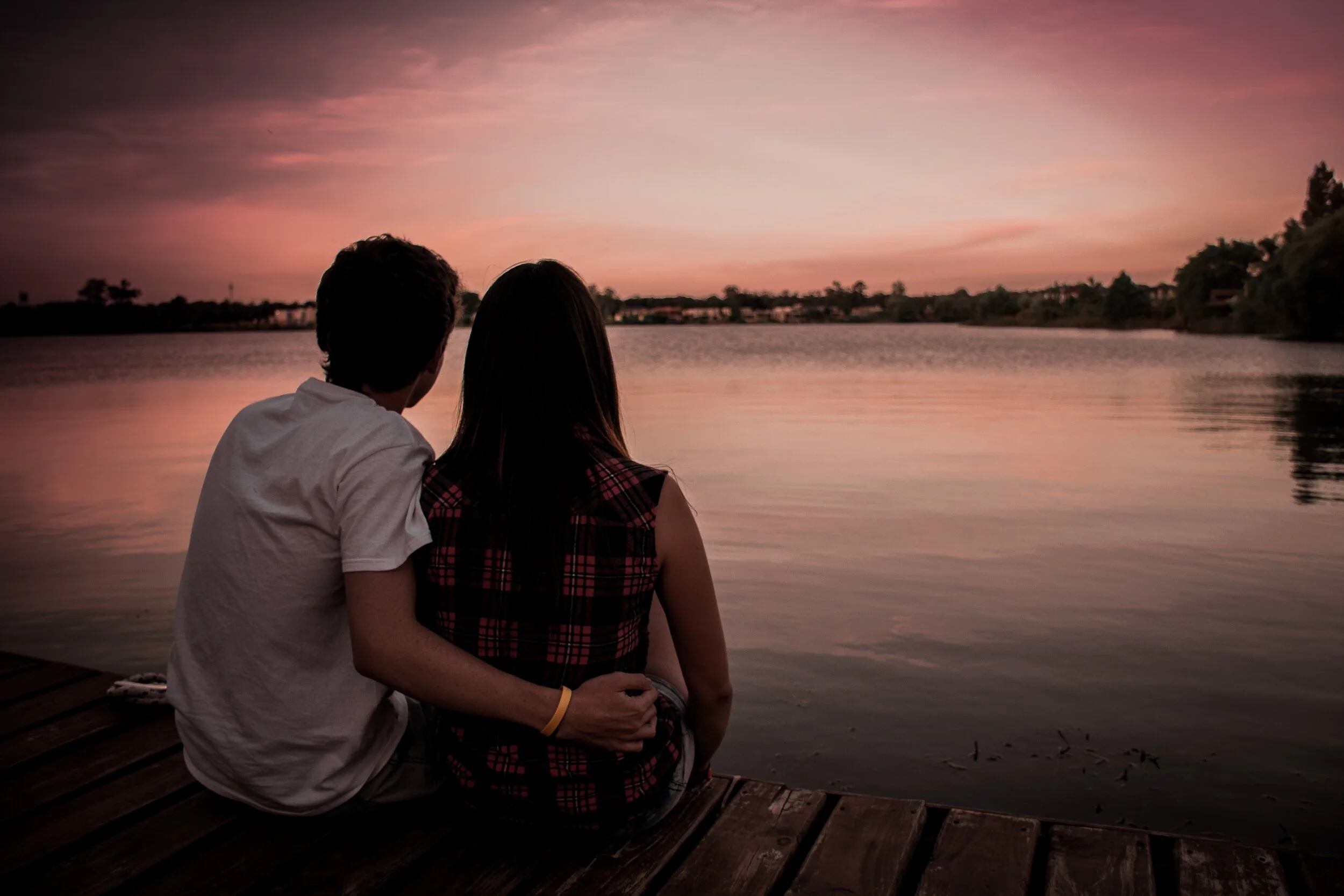 Couple sitting on a dock watching the sunset over a lake.