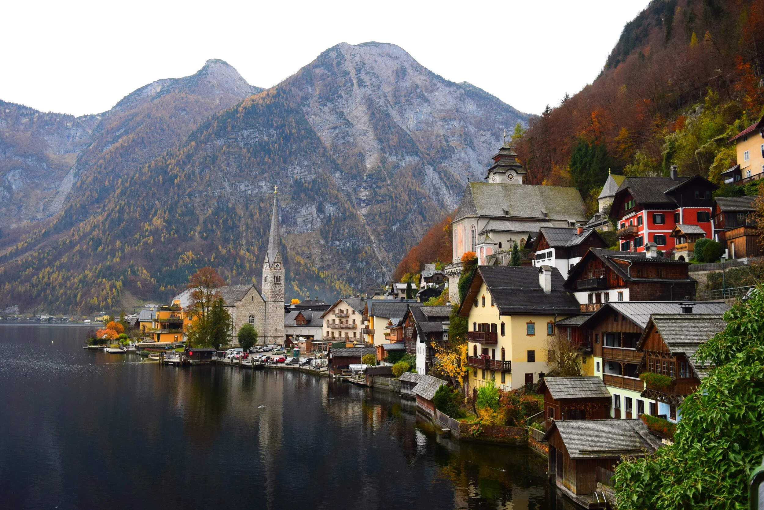 Scenic view of a lakeside village with traditional Alpine architecture, featuring colorful houses, a church with a tall steeple, and mountains in the background.