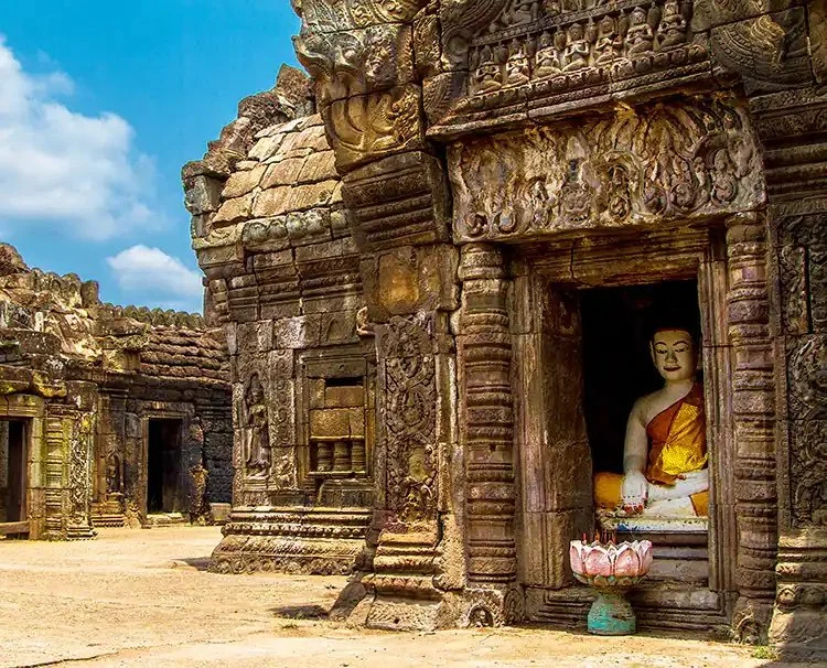 Ancient stone temple with intricate carvings and a seated Buddha statue inside, bright sky background.