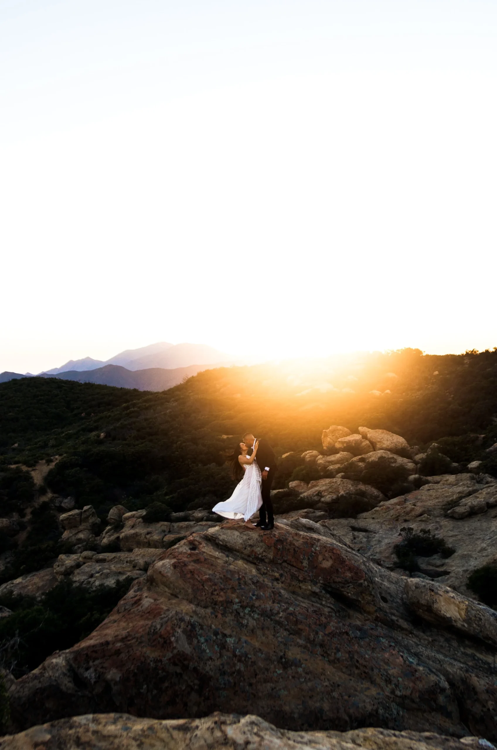 A couple embracing on a rocky hill at sunset.