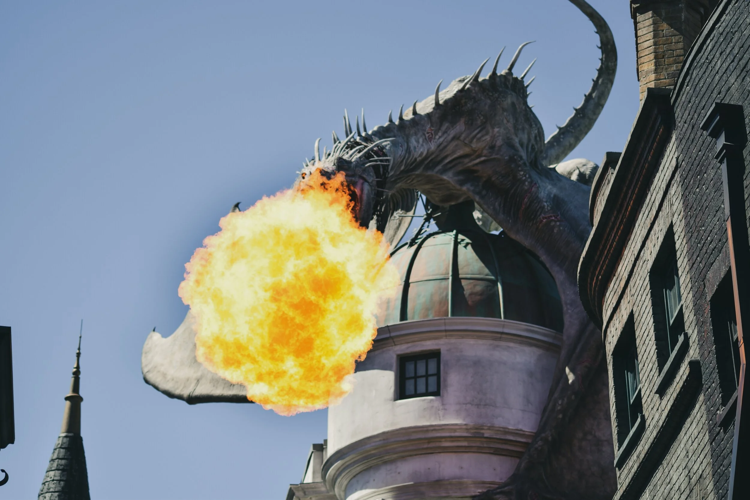 A dragon statue breathing fire atop a building against a clear blue sky.