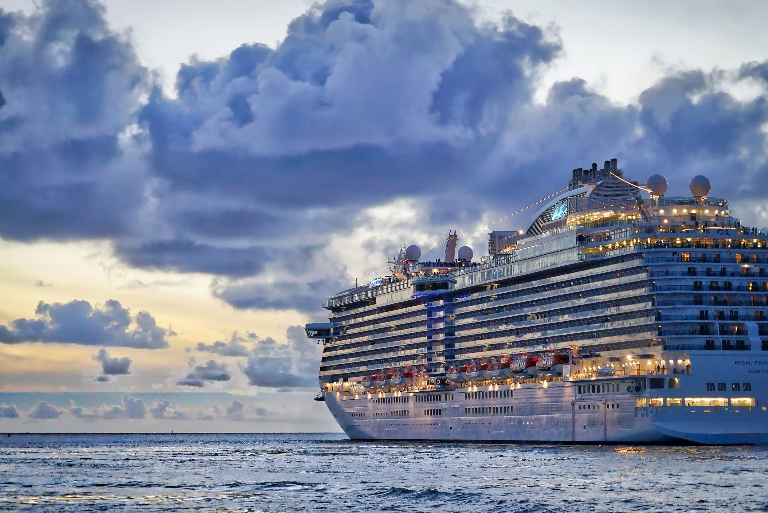 Cruise ship at sea during sunset with clouds in the sky.