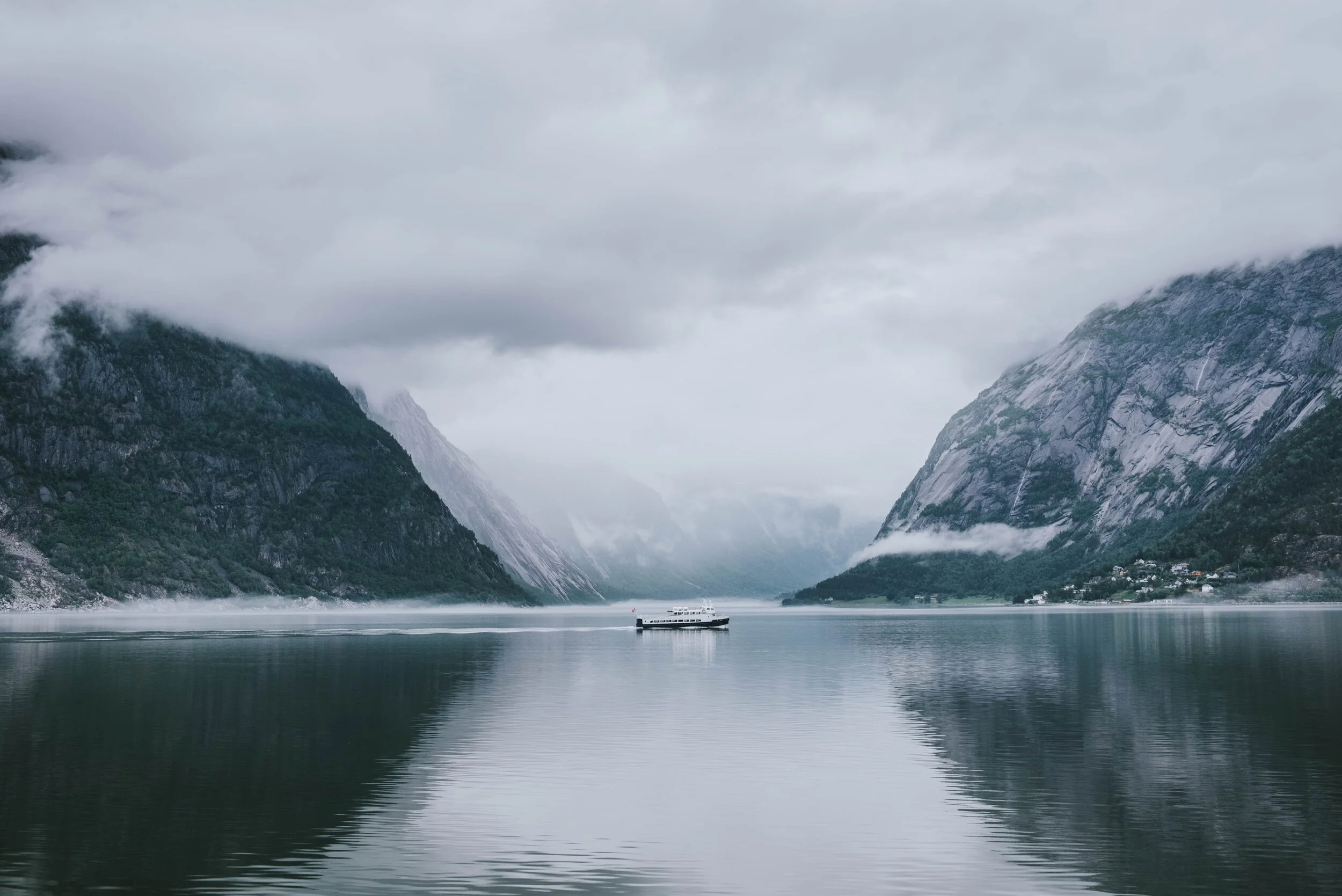 A scenic fjord with a boat and misty mountains in the background.