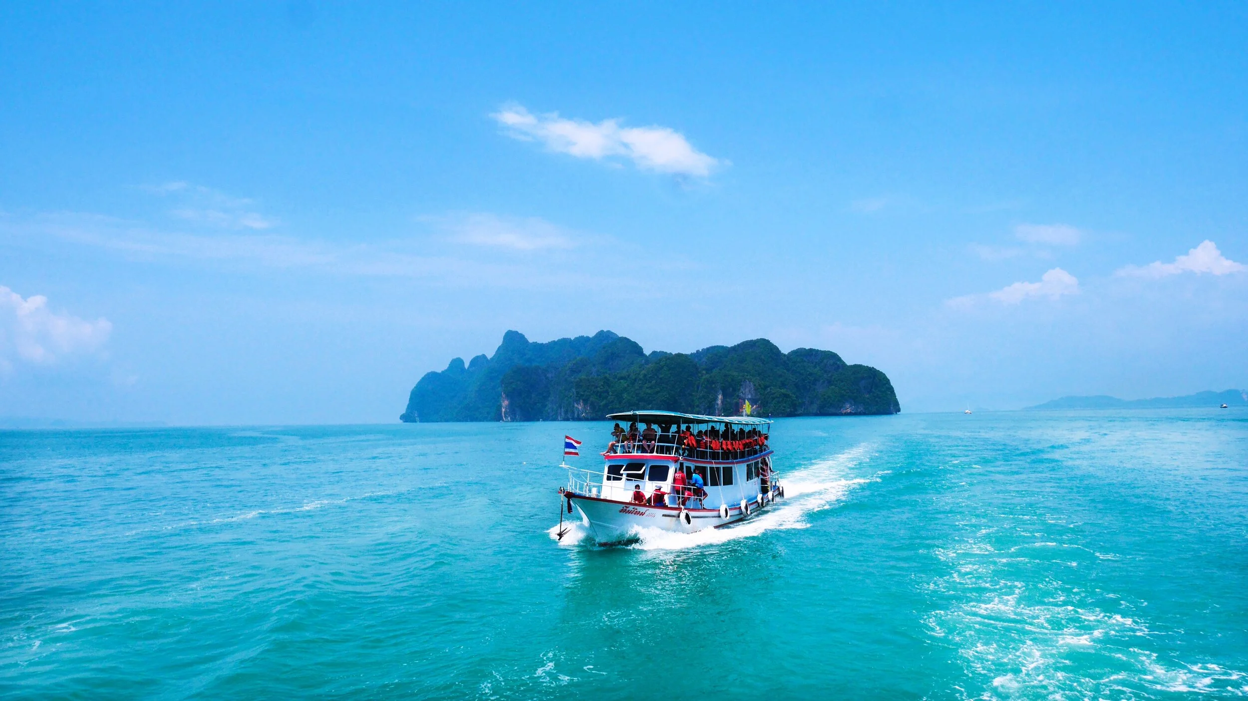 Tour boat in turquoise sea near a lush green island under a clear blue sky.